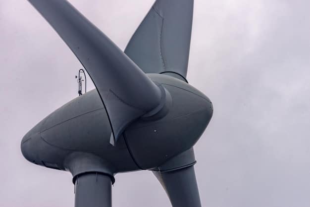 A close-up shot of a modern, sleek wind turbine with its blades silhouetted against a vibrant sunset. The turbine is set in a rural landscape with rolling hills, emphasizing the natural integration of wind energy into the environment.