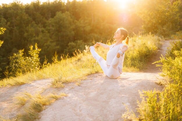 A woman practicing yoga outdoors at sunrise. She is in a relaxed pose, her face serene and focused. The soft morning light highlights the natural glow of her skin.