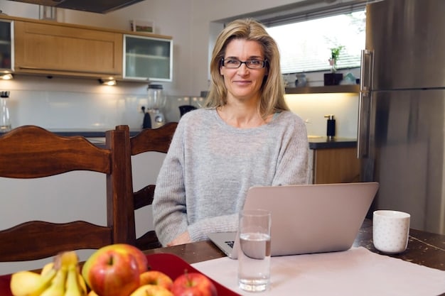 A woman in her late 40s sitting comfortably at a table, smiling as she prepares a healthy meal. The table is filled with colorful vegetables, fruits, and whole grains. She appears to be enjoying the process of cooking and maintaining a healthy lifestyle.