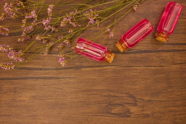 A top-down still life of different skincare product ingredients laid out on a wooden table, items include rose petals, seaweed, seeds and essential oil bottles.